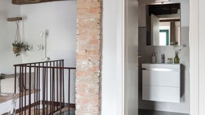 A modern bathroom with a white sink, mirror, and a brick accent wall. - Il Borghetto - The House of Elba, rooftop panoramic terrace (Castelnuovo dell'Abate)