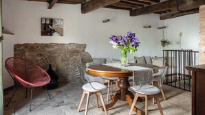 A rustic dining area with a round wooden table, clear chairs, a red chair, and a vase of purple flowers. - Il Borghetto - The House of Elba, rooftop panoramic terrace (Castelnuovo dell'Abate)