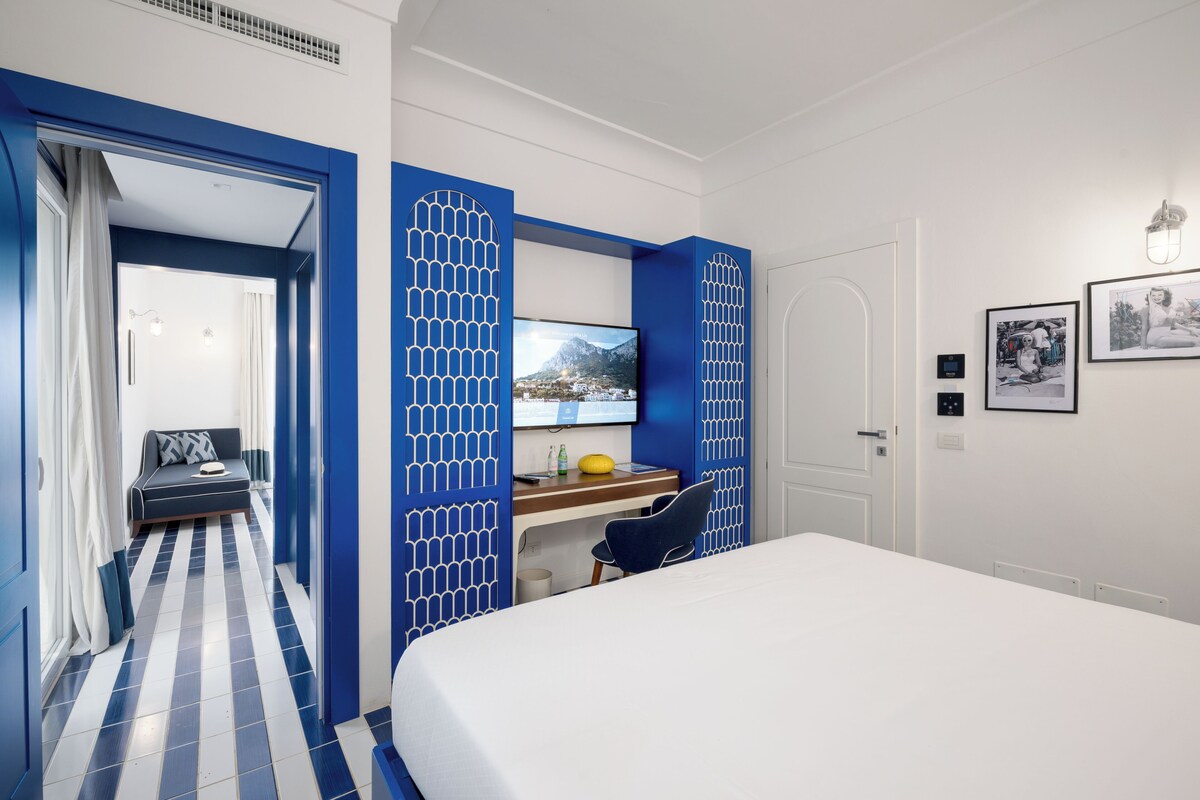 A hotel room with a bed, desk, chair, and a TV on the wall.