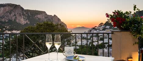 A table with two wine glasses and a menu, overlooking a coastal cityscape at sunset.