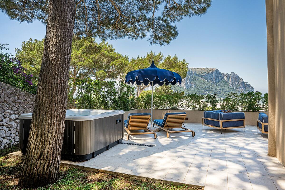 Une terrasse extérieure avec un jacuzzi, deux chaises longues et un parasol bleu.