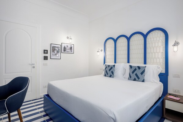A bedroom with a bed, a chair, a nightstand, and wall-mounted light fixtures. - Villa Lia Hotel Capri (Capri)