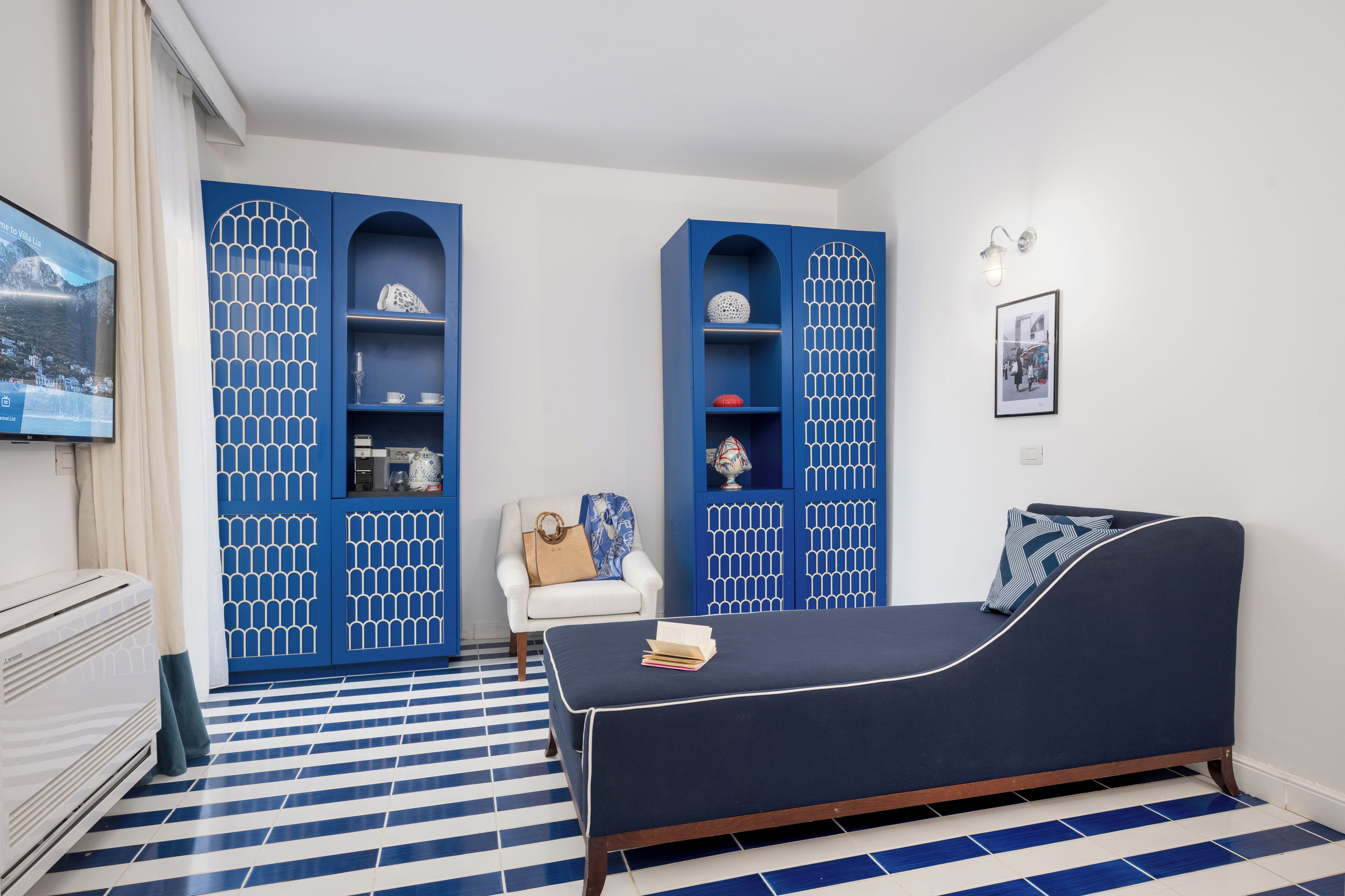 A room with a blue sofa, a white armchair, and a TV on the wall.