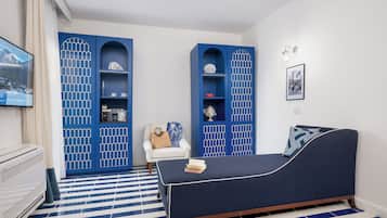 A room with a blue sofa, a white armchair, and a TV on the wall.