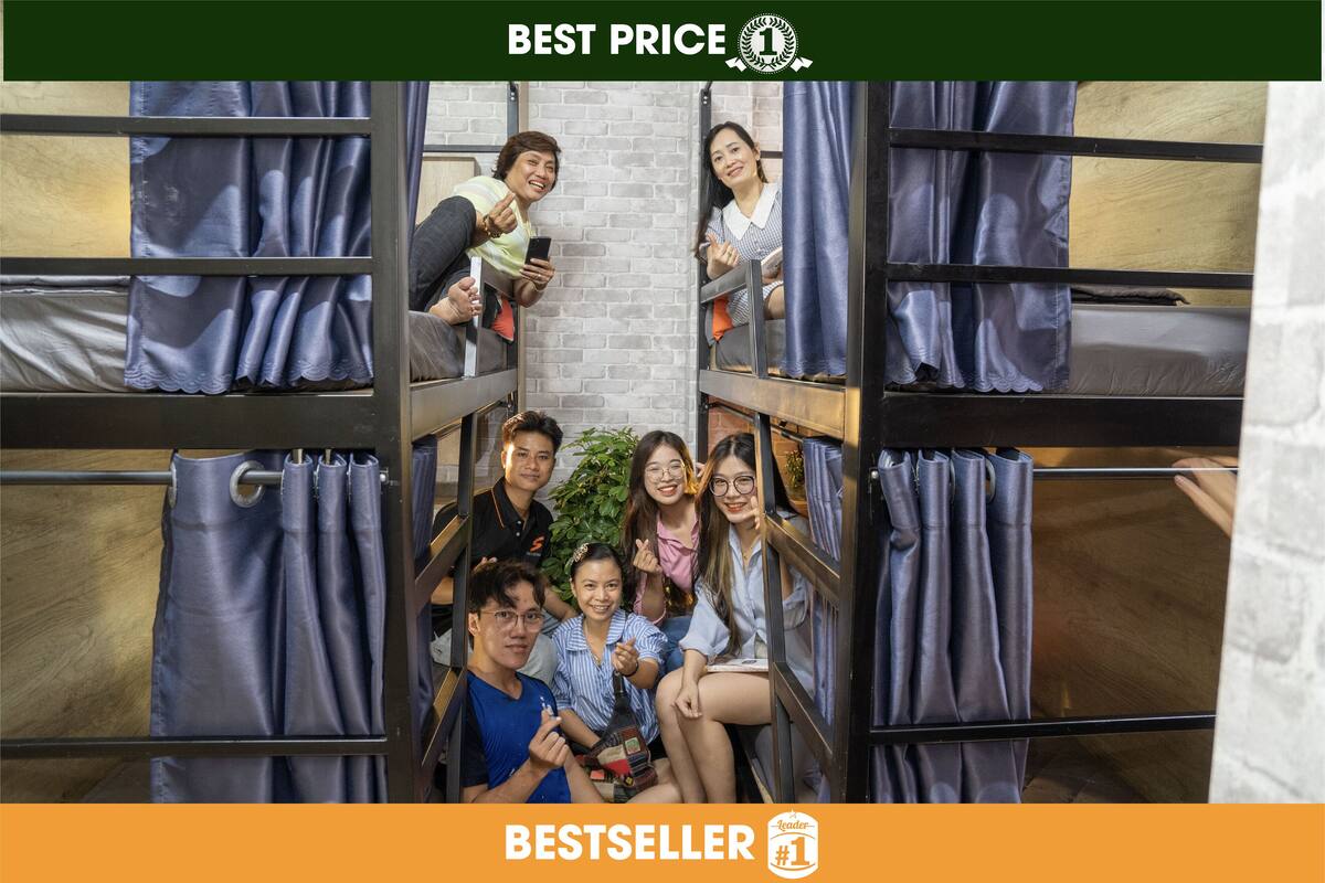 A group of people in a bunk bed room with curtains, a brick wall, and a wooden floor.