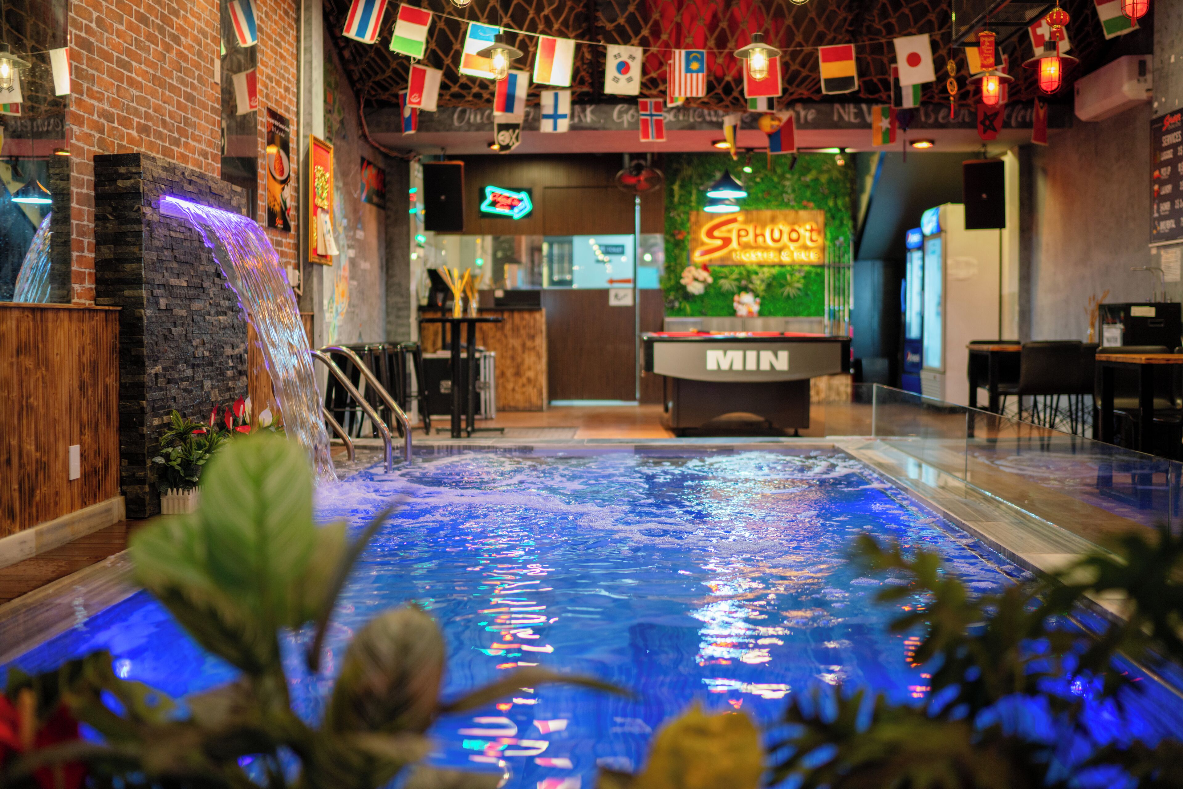 An indoor pool area with a water feature, a neon sign, and a bar area.