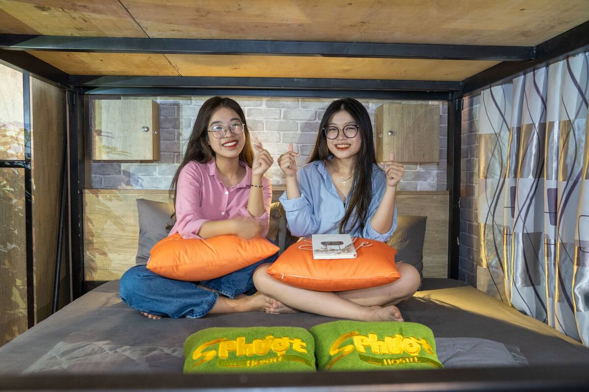 Two people sitting on a bed with pillows, a book, and a blanket.