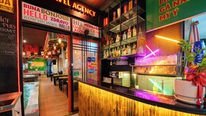 A bar area with a wooden counter, shelves with bottles, and a neon sign. - S Phuot Da Nang Hostel (Da Nang)