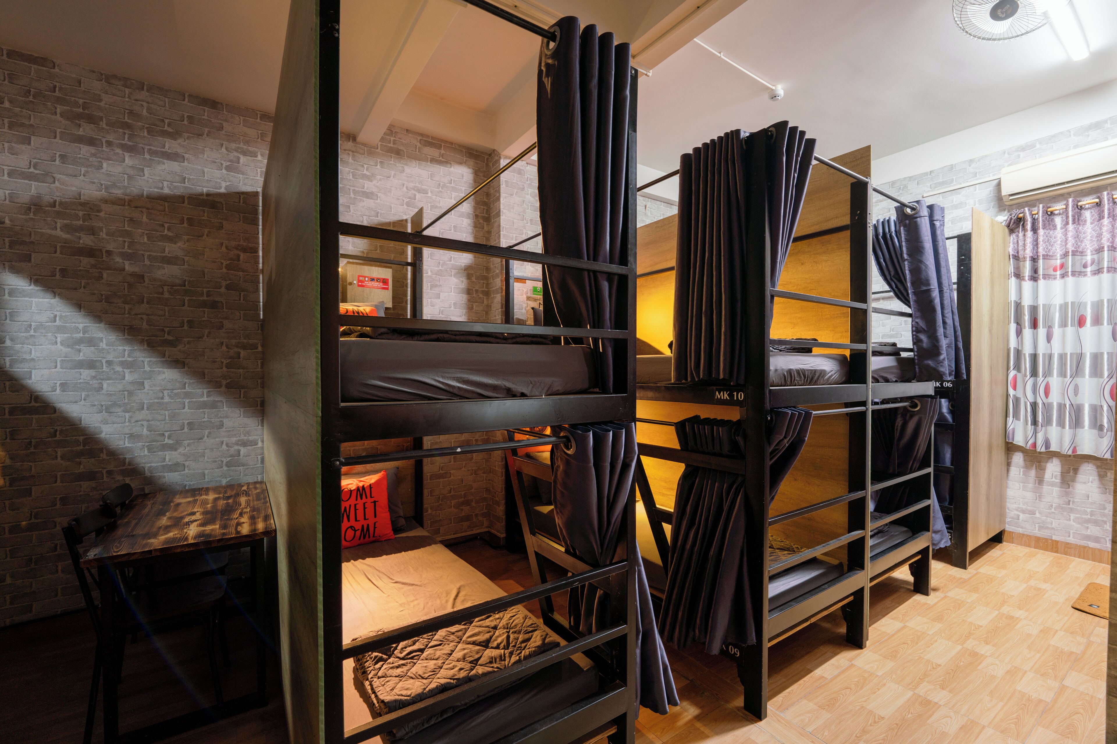 A bunk bed room with a brick wall, a wooden table, and a window with curtains.