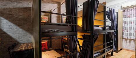 A bunk bed room with a brick wall, a wooden table, and a window with curtains.