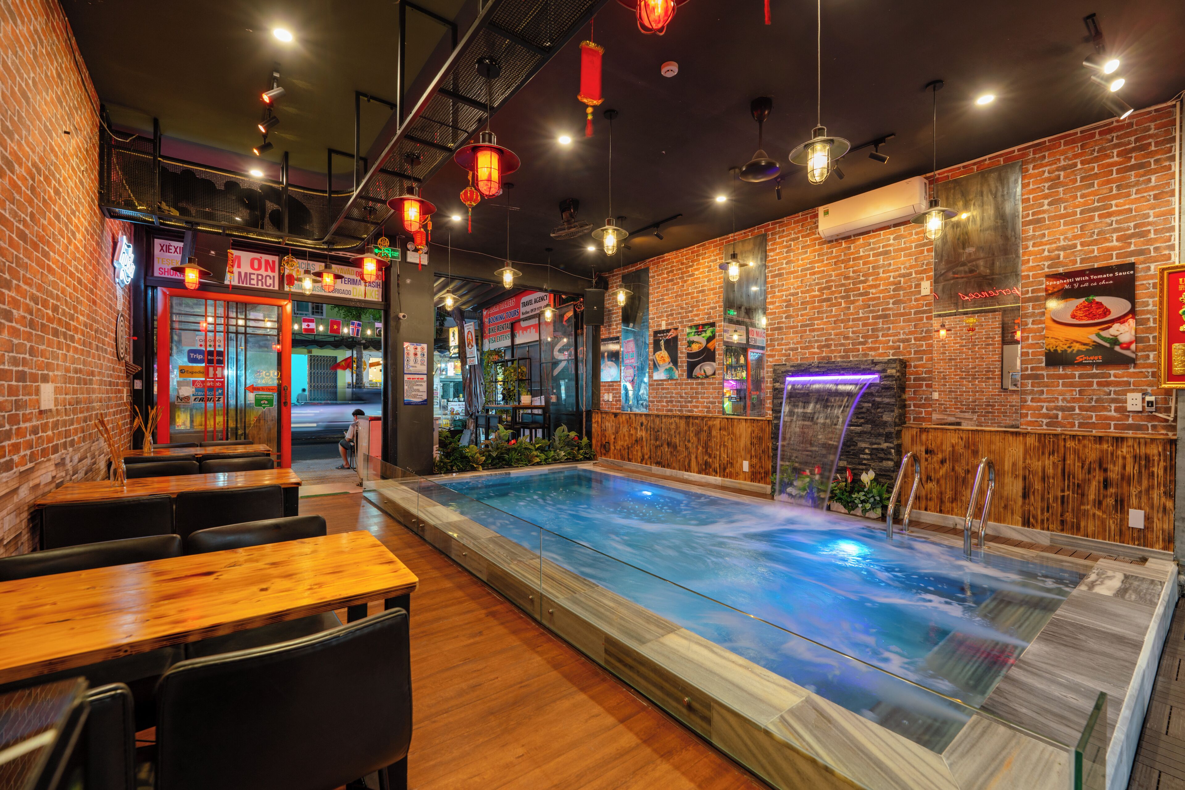 Un restaurante con zona de piscina, paredes de ladrillo, mesas de madera y luces colgantes.