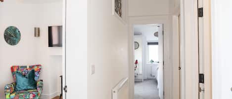Un couloir avec un fauteuil à motifs, une horloge murale et un luminaire suspendu.