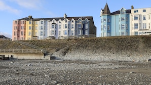 A row of colorful seaside buildings with a rocky beach in the foreground. - The Nook (Criccieth)