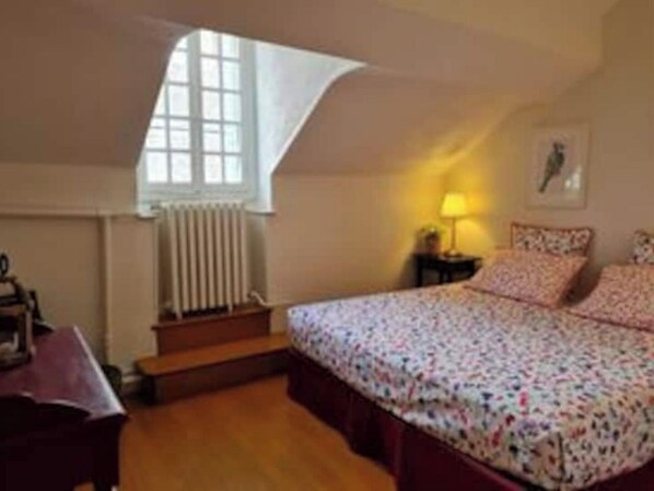 Une chambre à coucher avec un lit, une fenêtre, un radiateur, une table de chevet et une lampe.