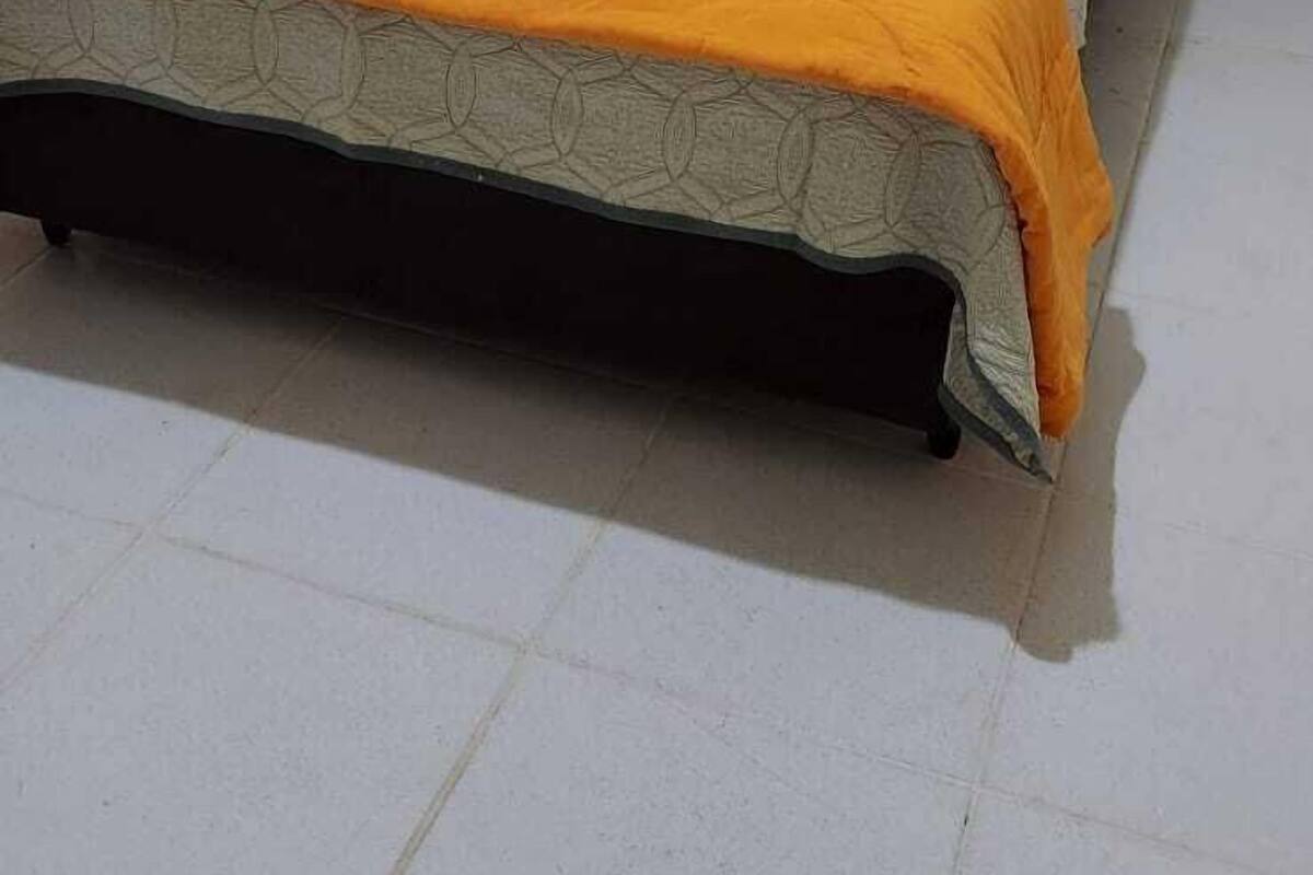 Una cama individual con una colcha naranja en una habitación con paredes blancas y un ventanal pequeño.
