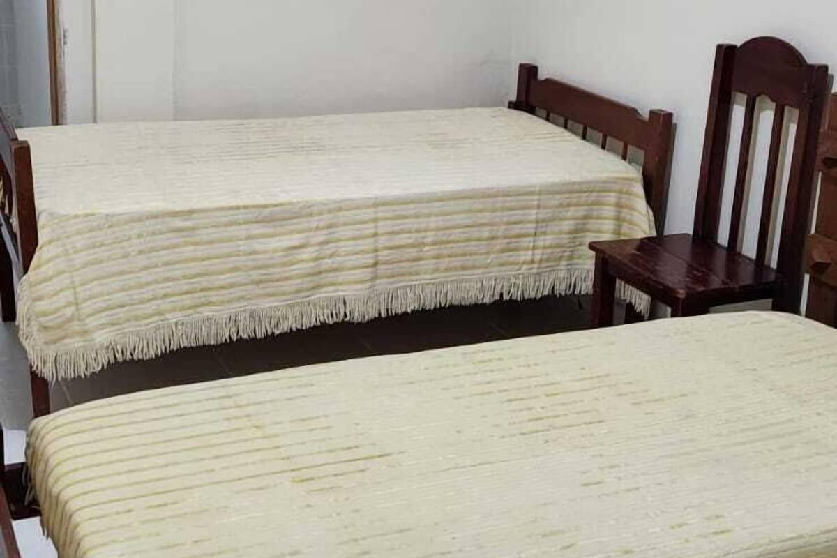 Dos camas individuales con cabeceros de madera y ropa de cama color beige en una habitación con paredes blancas y suelo de baldosas.