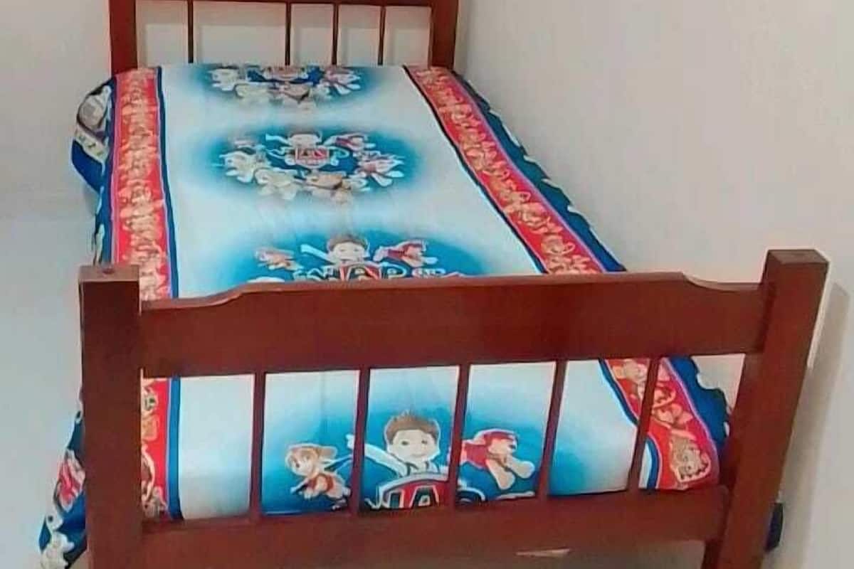 Una cama de madera pequeña con una colcha azul y roja que muestra personajes de dibujos animados.