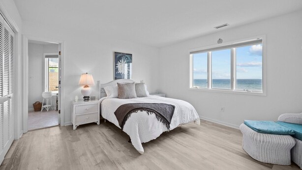 Une chambre spacieuse avec un grand lit, une table de chevet, une lampe, une fenêtre donnant sur la mer et une porte menant à une autre pièce.