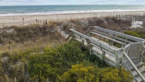 Une promenade en bois qui mène à une plage de sable et offre une vue sur l’océan.
