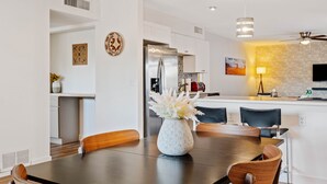 A modern kitchen with white cabinets, a stainless steel refrigerator, and a dining area with a wooden table and chairs. - Mountain Views | Hiking & Adventure (Phoenix)