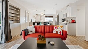 A modern living room with a red sofa, a wooden coffee table with a plant, and a kitchen in the background. - Mountain Views | Hiking & Adventure (Phoenix)