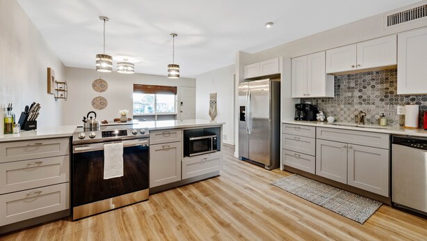 A modern kitchen with stainless steel appliances, white cabinetry, and a wooden floor. - Mountain Views | Hiking & Adventure (Phoenix)