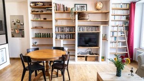 A living room with a wooden dining table, chairs, a TV, bookshelves, and a coffee table with flowers. - Peace and comfort in the heart of the city (Draguignan)