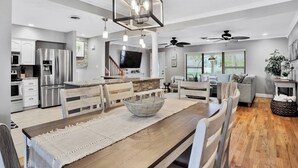 A modern kitchen with stainless steel appliances, a dining area with a wooden table and chairs, and a living room with a sofa and a TV. - Private Resort Home with Pool & Hot Tub (Indian Harbour Beach)