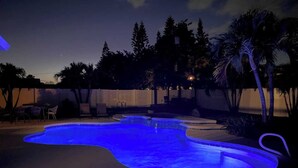 A swimming pool with a blue light at night, surrounded by palm trees and chairs. - Private Resort Home with Pool & Hot Tub (Indian Harbour Beach)