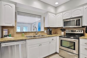 A modern kitchen with white cabinetry, stainless steel appliances, a granite countertop, and a window above the sink.