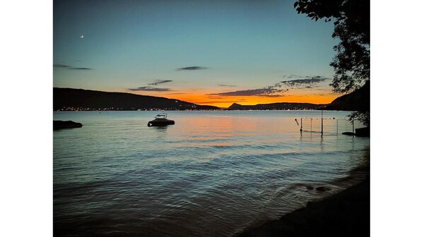 A calm lake at sunset with a boat in the center, surrounded by hills and a clear sky. - Loft Mandallaz - In the heart of the city (Annecy)