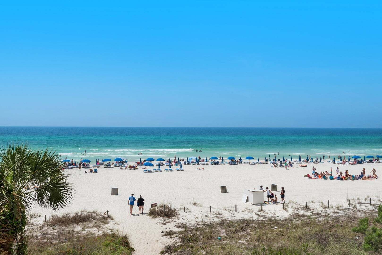 A beach with white sand, blue umbrellas, and people relaxing.