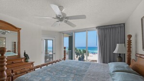 Une chambre avec un grand lit, un ventilateur de plafond, une commode et une vue sur la plage.
