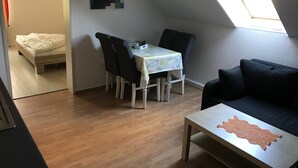 Habitació petita i ben il·luminada amb una taula de dinar, cadires, un sofà i un llit.