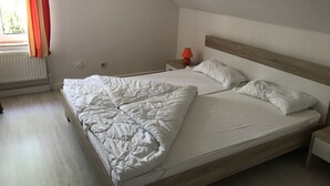 Un dormitori amb un llit de fusta, roba de llit blanca, una tauleta de nit amb una làmpada i una finestra amb cortines.