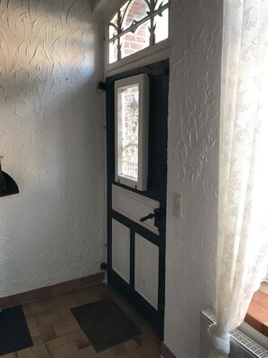 Une pièce aux murs blancs à texture, une fenêtre ornée de vitraux, une porte à cadre noir et un radiateur.