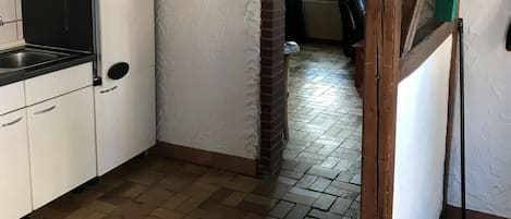 Une cuisine avec des armoires blanches, un plan de travail noir et un plancher en bois. Une arche en briques mène à une autre pièce.