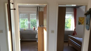 Ein Flur, der zu einem Schlafzimmer führt, mit einem Bett, einem Heizkörper und einem Fenster mit Vorhängen.