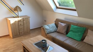 Ein gemütliches Wohnzimmer mit Holzboden, einem braunen Ledersofa mit Kissen, einem kleinen Holztisch und einer Kommode mit Schubladen.