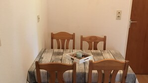Taula de dinar amb quatre cadires de fusta, un quadre al mur i una porta al fons.