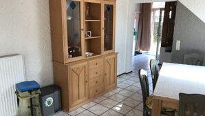 A room with a wooden cabinet, a radiator, a trash bin, and a dining table with chairs.
