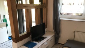 A small room with a TV on a wooden stand, a blue folder, a small sofa, and a window with curtains.