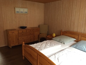 Ett sovrum med träpanel på väggarna, innehållande en säng, en byrå, en stol och ett sängbord med en lampa.