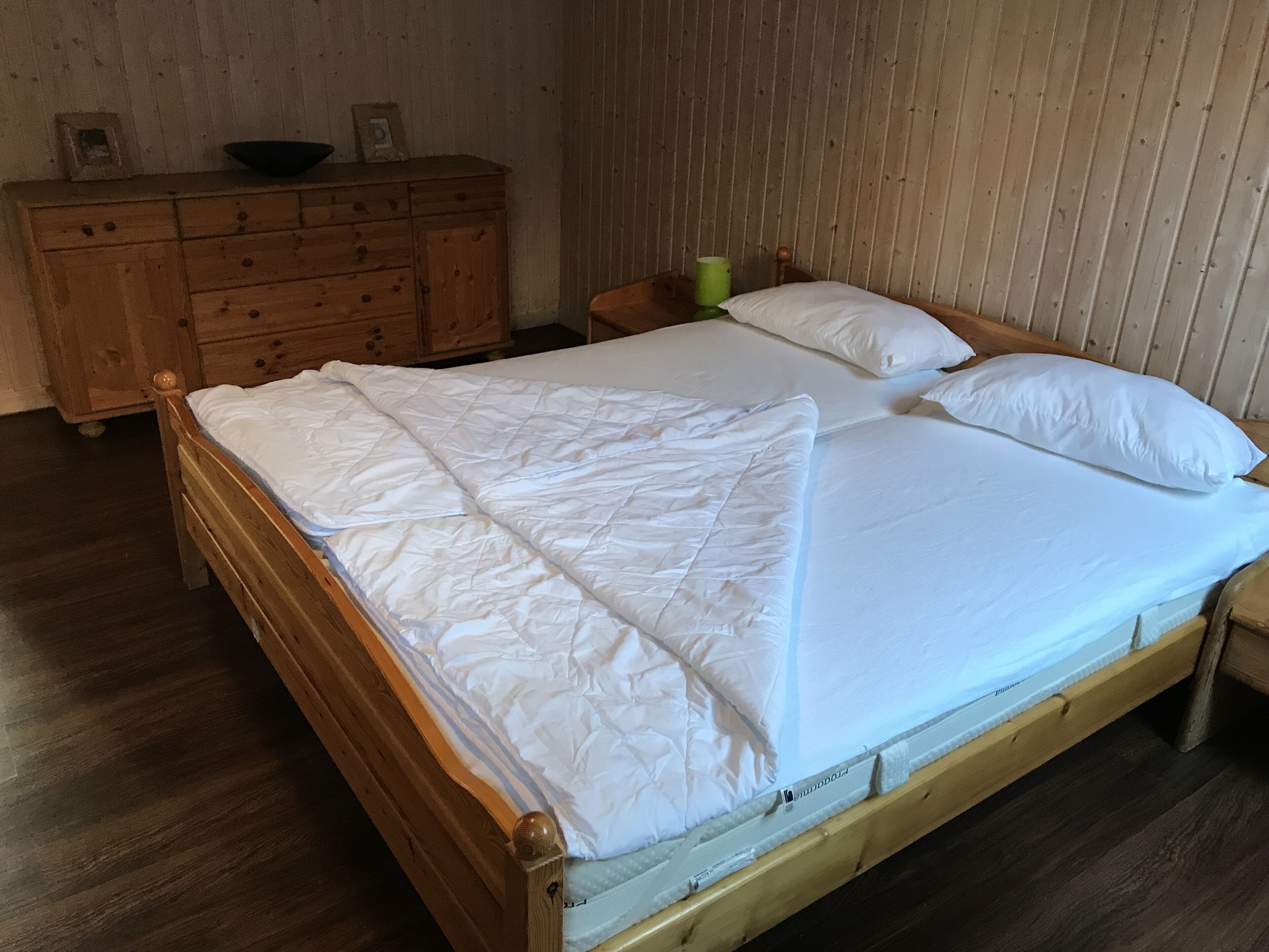 A wooden bed with white bedding in a room with wooden walls and a wooden dresser.