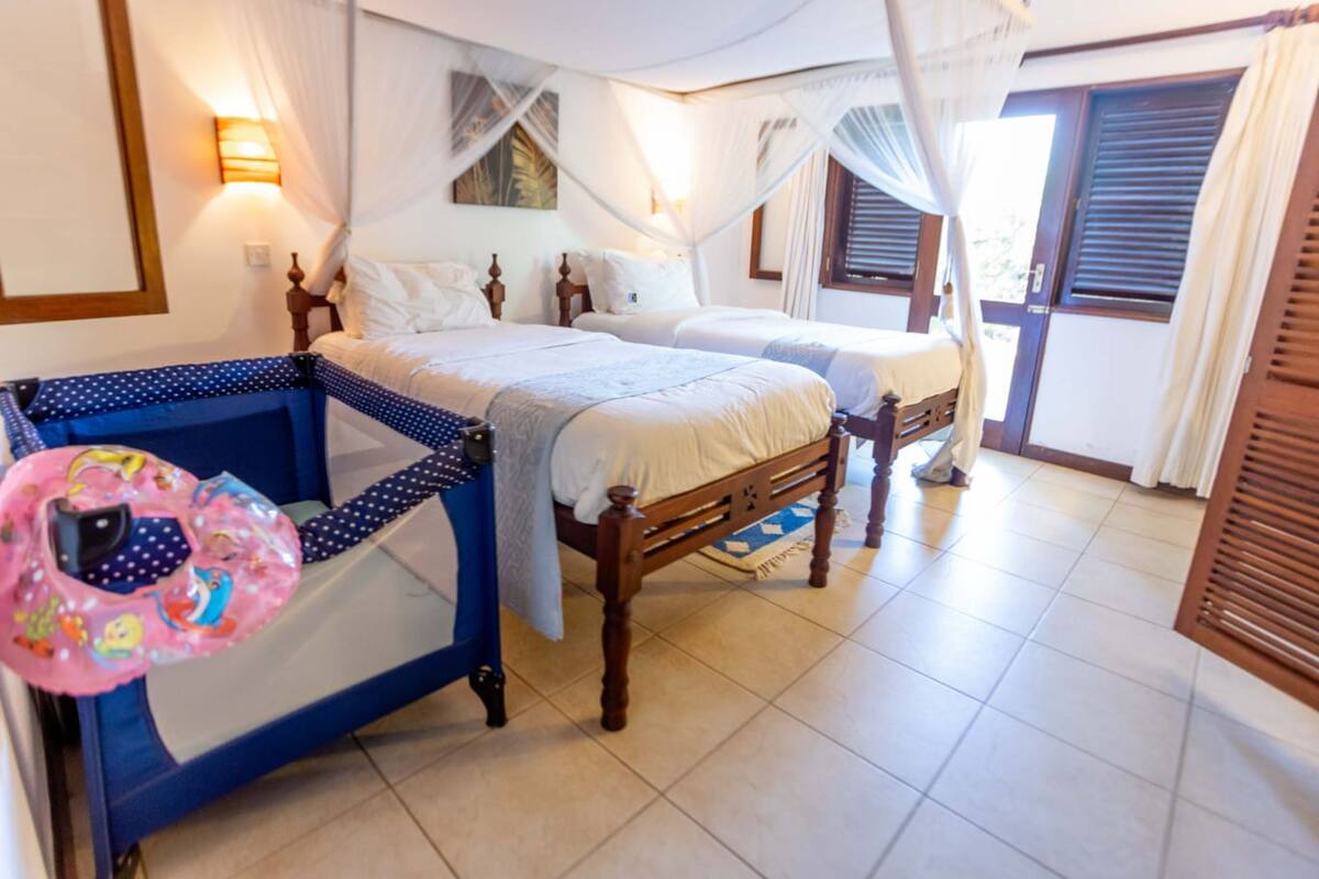 Een slaapkamer met twee bedden, een nachtkastje, een raam met luiken en een gordijn.