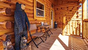 En stuga av trä med en veranda, två stolar, ett bord och två björnstatyer.