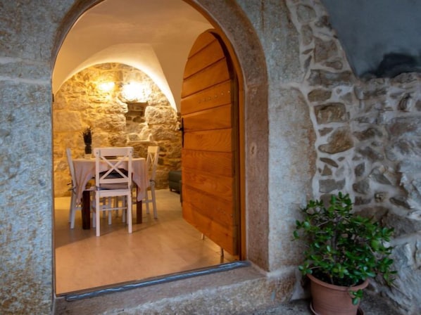 A stone-walled room with a wooden door, a table with chairs, and a potted plant.