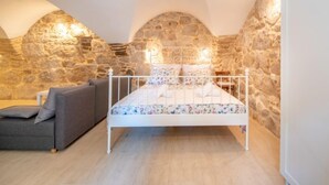 A bedroom with a stone wall, a bed, a sofa, and a small table. - Vacation home Dvor by Interhome (Crikvenica)