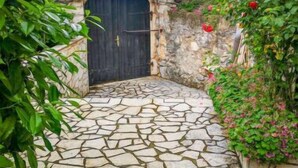 A stone pathway leading to a dark wooden gate, surrounded by lush greenery and flowering plants. - Vacation home Dvor by Interhome (Crikvenica)