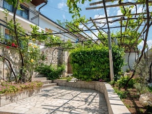 Un patio empedrado con una pérgola, plantas trepadoras y un muro de piedra.